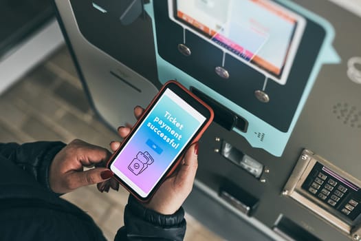 Woman buying ticket at ticket machine paying using mobile payment app on smartphone. Female buying bus public transpoort ticket in vending machine. Person purchasing car parking ticket using mobile phone