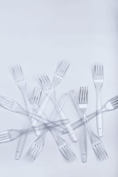 Plastic forks scattered over white background. Collecting plastic waste to recycling. Concept of plastic pollution and too many plastic waste. Copy space at the top