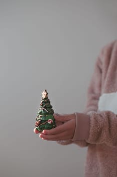 Girl wearing warm sweater holding Christmas tree figurine