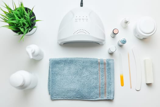 Cosmetic products set, nail hybrid gels, UV lamp, green leaves, blue towel on white table. Spa, manicure, skin care concept. Flat lay, overhead view