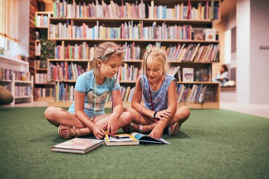Two primary students reading books in school library. Schoolgirls learning from books. Pupils doing homework. Children having fun in school club. Back to school