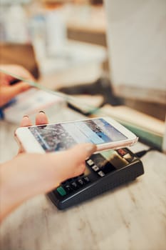 Woman paying for medicines at pharmacy using contactless method of payment via mobile phone. Woman using new way of payments