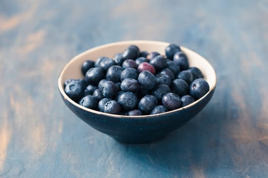 Small bowl full of fresh blueberries put on table painted in blue