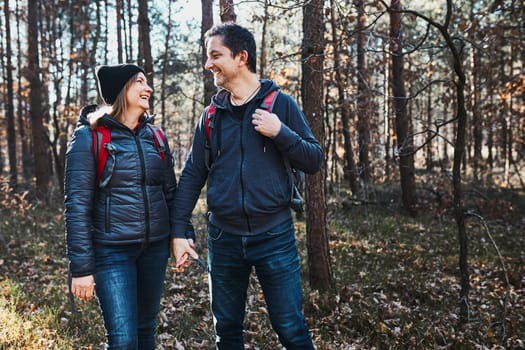 Couple holding hands enjoying trip while vacation day. Hikers with backpacks walking on forest path on sunny day. Active leisure time close to nature