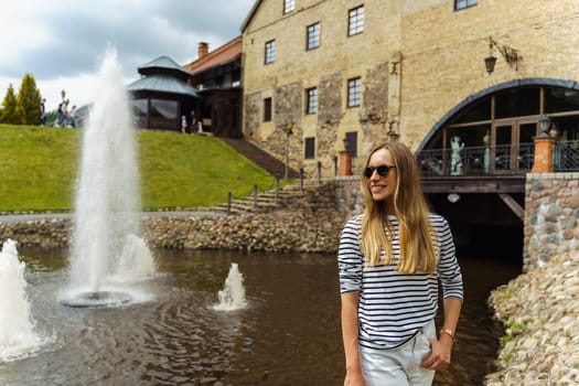 Smiling long-haired woman in a striped jumper near the fountain in summer.