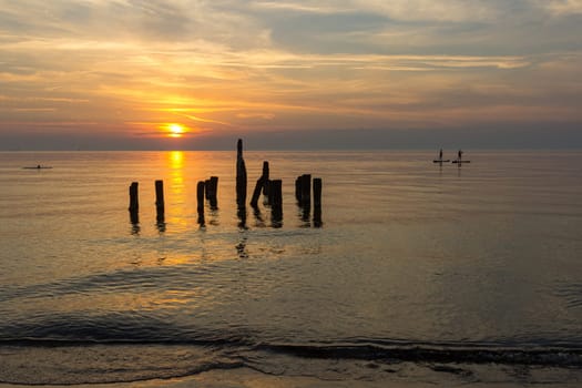 Sunset in the Baltic Sea at the old pier in Ventspils, Latvia. Silhouettes of surfers.