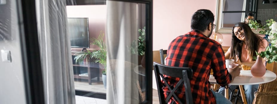 Young diverse loving couple eating croissant and talks together at home in breakfast time. Communication and relationship