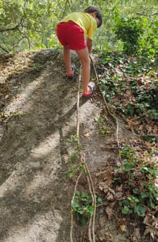 Child boy climbing up a rock with the help of an ivy branch. Summer camp por children concept