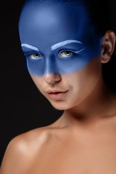 Portrait of a young woman who is posing covered with blue paint in the studio on a black background.