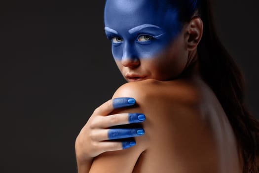 Portrait of a young woman who is posing covered with blue paint in the studio on a black background. girl&#39 s hand  painted blue