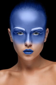 Portrait of a young woman who is posing covered with blue paint in the studio on a black background. Girl has blue lips and white eyebrows