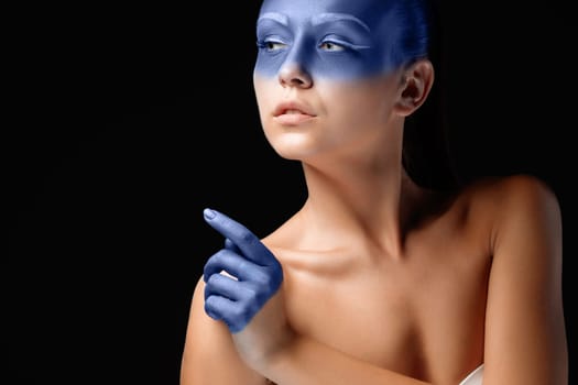 Portrait of a young woman who is posing covered with blue paint in the studio on a black background. girl&#39 s hand  painted blue