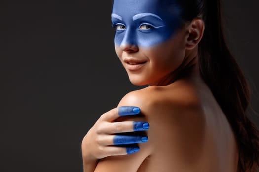 Portrait of a young woman who is posing covered with blue paint in the studio on a black background. girl&#39 s hand  painted blue