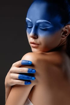Portrait of a young woman who is posing covered with blue paint in the studio on a black background. girl&#39 s hand  painted blue