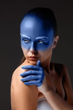 Portrait of a young woman who is posing covered with blue paint in the studio on a black background. girl&#39 s hand  painted blue