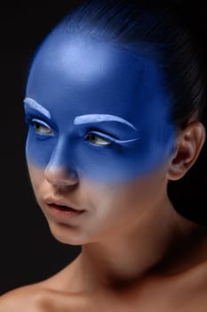 Portrait of a young woman who is posing covered with blue paint in the studio on a black background.