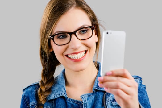 Beautiful woman smiling and taking a selfie, isolated over a grey background
