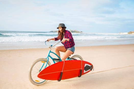Surfer young woman riding her bicycle on the beach