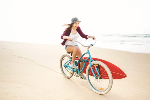 Surfer young woman riding her bicycle on the beach