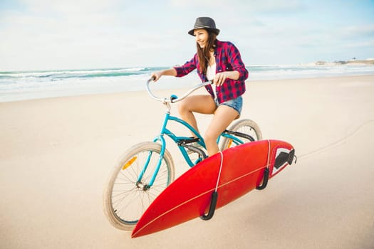 Surfer young woman riding her bicycle on the beach