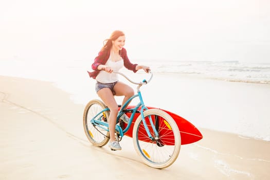 Surfer young woman riding her bicycle on the beach
