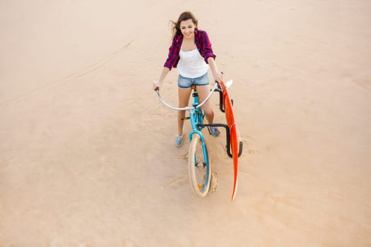 Surfer young woman riding her bicycle on the beach