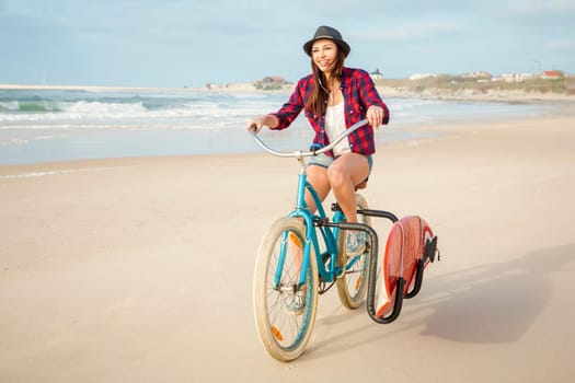 Surfer young woman riding her bicycle on the beach