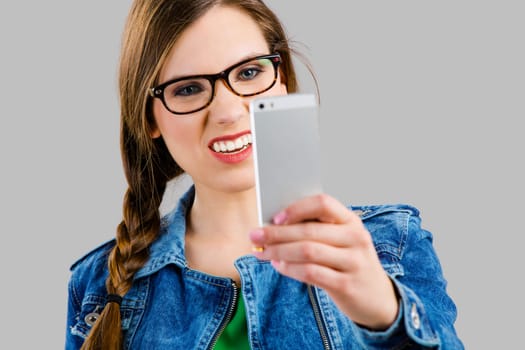 Beautiful woman smiling and taking a selfie, isolated over a grey background
