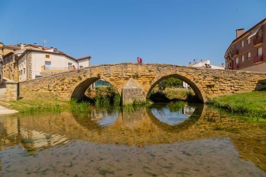 Navarre, Spain, 26 August, 2022: Pilgrims walking over the medieval bridge part of the pilgrim route the Camino de Santiago the way of St James in the village of Villatuerta. Spain