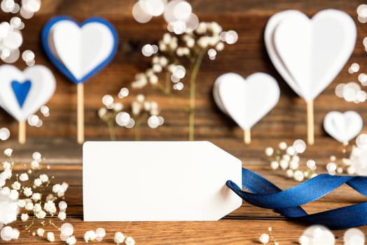 Label With Copy Space For Your Free Text. White Festive And Atmospheric Decoration Like Hearts, Flowers And A Blue Bow. Vintage, Wooden Background.