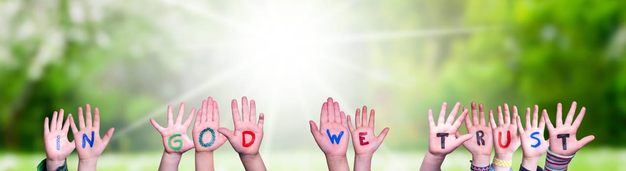 Children Hands Building Colorful English Word In God We Trust. Sunny Green Grass Meadow As Background.