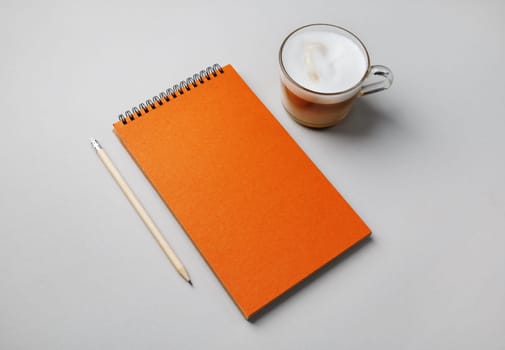 Blank orange notepad, coffee cup and pencil on gray paper background.