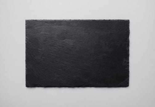 Photo of black stone slate plate on gray paper background. Copy space for text. Flat lay.