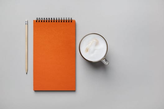 Photo of blank orange sketchbook, coffee cup and pencil on gray paper background. Flat lay.