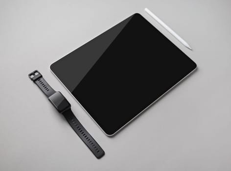 Digital tablet with blank black screen, fitness bracelet and stylus pen on gray paper background.