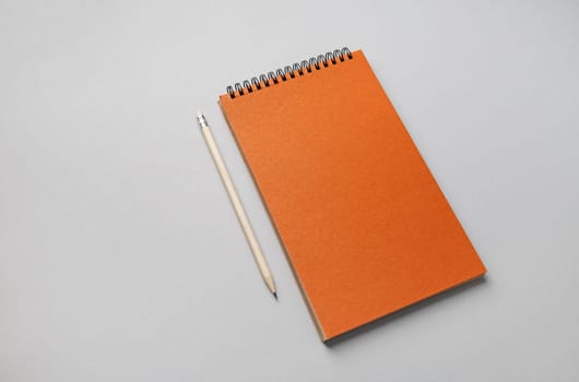 Photo of blank orange sketchbook and pencil on gray paper background.