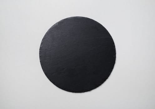 Photo of round slate plate on gray paper background. Copy space. Flat lay.