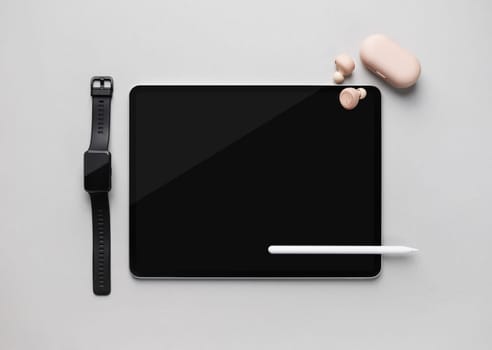 Modern digital tablet, stylus pen, smartwatch and headphones on gray paper background. Responsive design mockup. Top view. Flat lay.