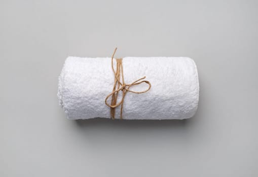 Rolled white towel tied with a rope on gray paper background.