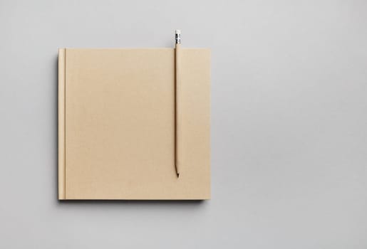 Blank closed book and pencil on gray paper background. Responsive design template. Copy space for text. Flat lay.