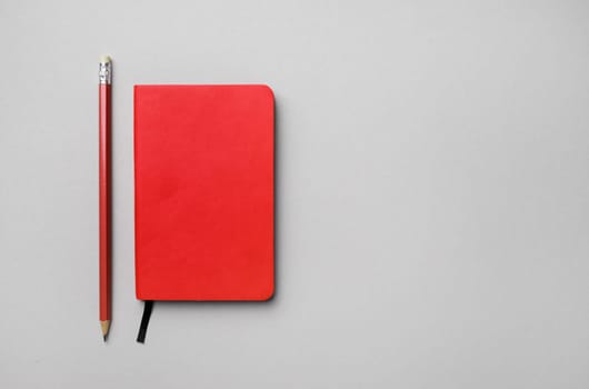 Photo of blank red notebook and pencil on gray paper background. Branding mock up. Space for text. Flat lay.