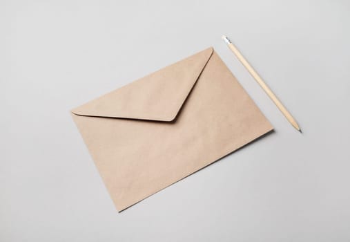 Blank kraft paper envelope and pencil on gray paper background. Mockup for your design.