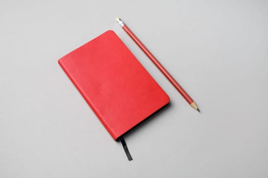 Photo of blank red notebook and pencil on gray paper background.