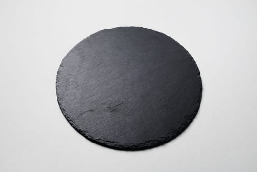 Black round stone slate plate on gray paper background.