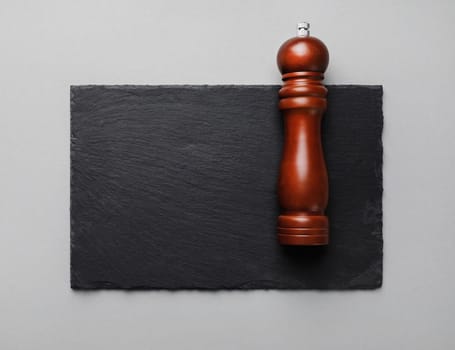 Photo of pepper mill and slate plate on gray paper background. Copy space. Flat lay.