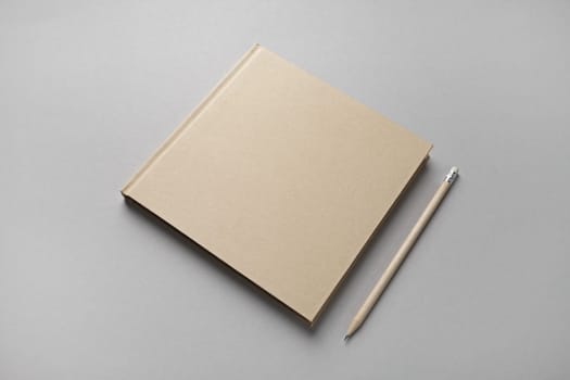 Photo of closed blank kraft brochure and pencil on gray paper background. Template for placing your design.