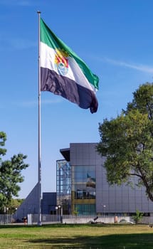 Merida, Spain - April 17th, 2023: Extremadura Region flag waving over blue sky. Lusitania Bridge roundabout, Merida, Spain
