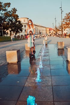 Teenager girl and her sister preschooler riding an electric scooter in the city center. Woman wearing the face mask to avoid virus infection and to prevent the spread of disease in time of coronavirus. Candid people, real moments, authentic situation