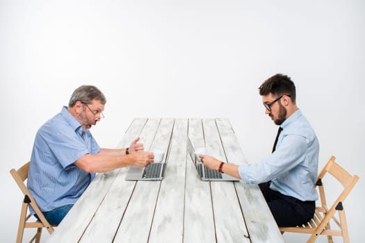 two colleagues working on project together on light gray background. They drinking coffee. happy man and jealous man. the concept of competition in the business