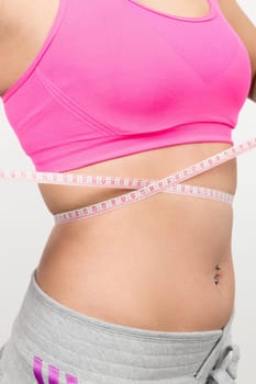 A young woman with a baunch navel piercing measures her waist with a band of measure